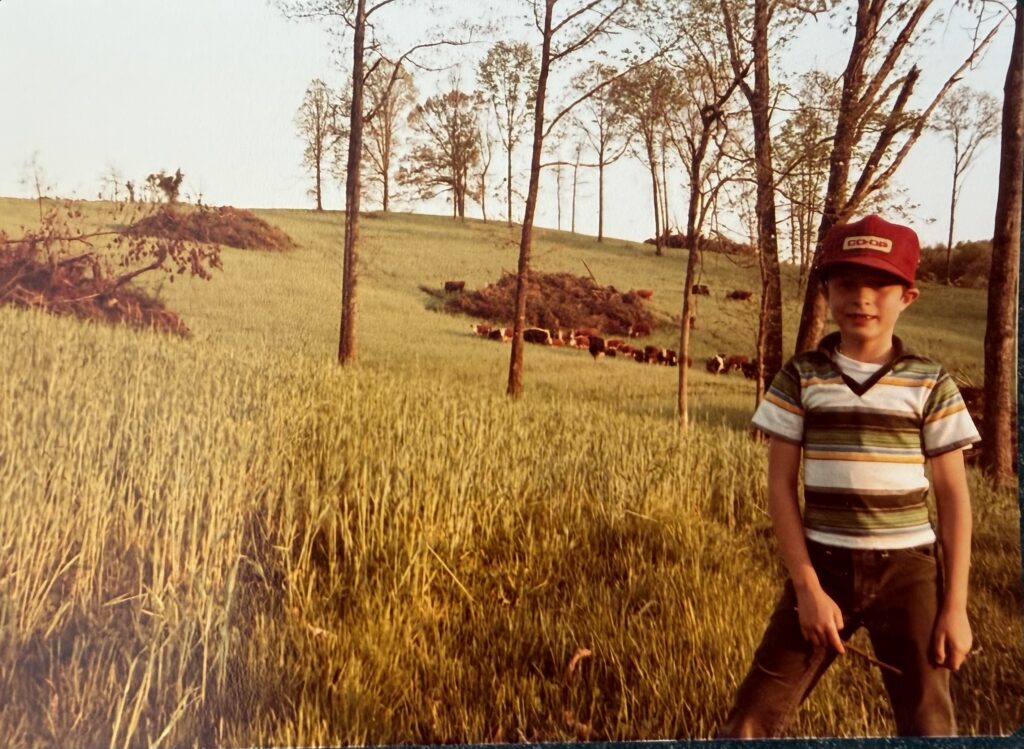 Generations of RiverView Family Farm captured in a vintage photo of Byron Williams standing in a pasture with cattle in the background.